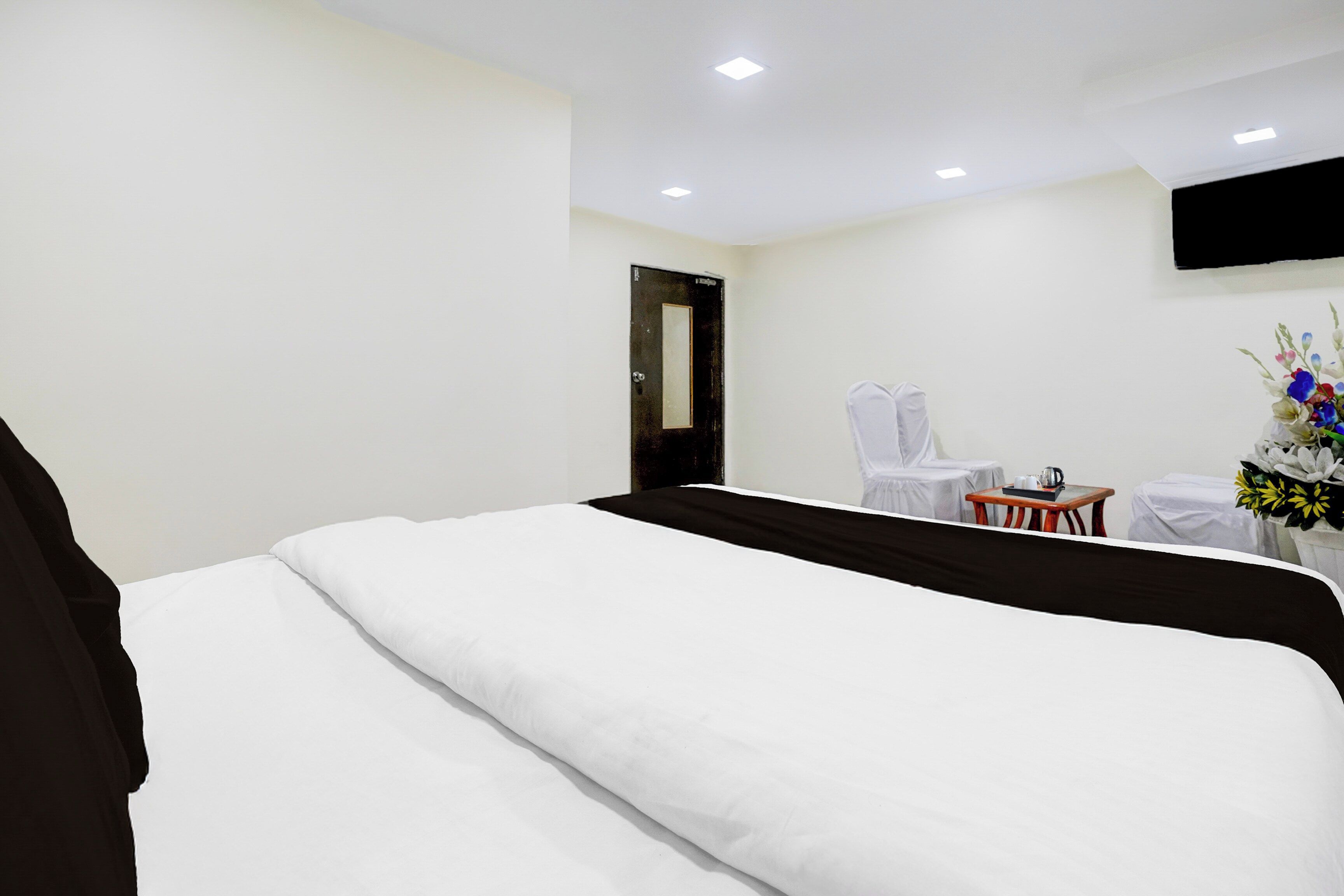 Habitación de hotel con cama, escritorio, silla, televisor de pantalla plana montado en la pared y un jarrón con flores.