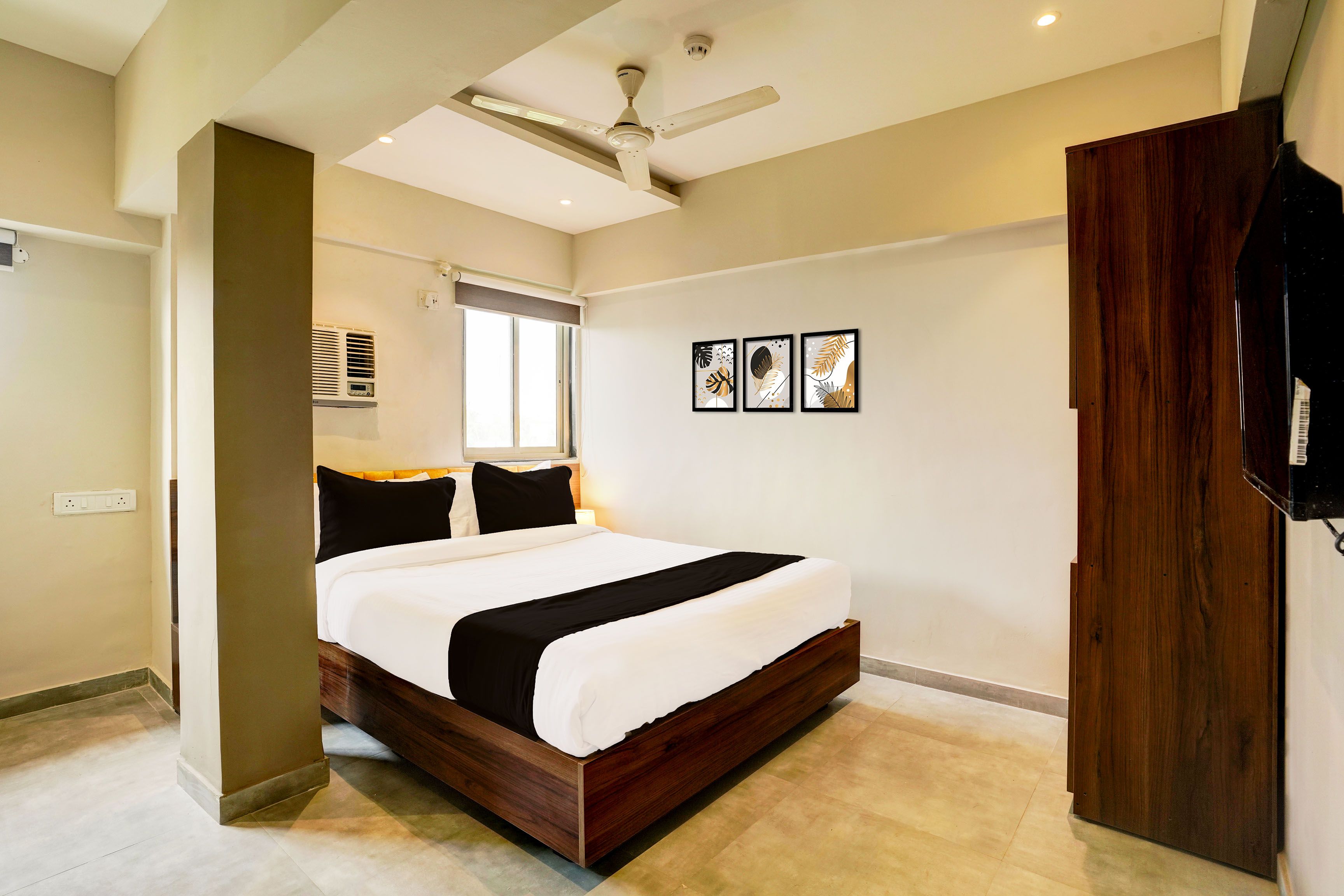 A bedroom with a bed, a ceiling fan, a window with blinds, a wall-mounted air conditioner, and framed artwork.