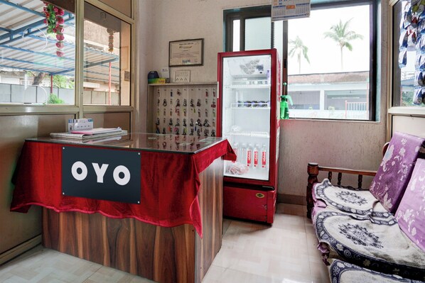 A reception desk with a sign, a refrigerator, a window with a view, and a patterned sofa.