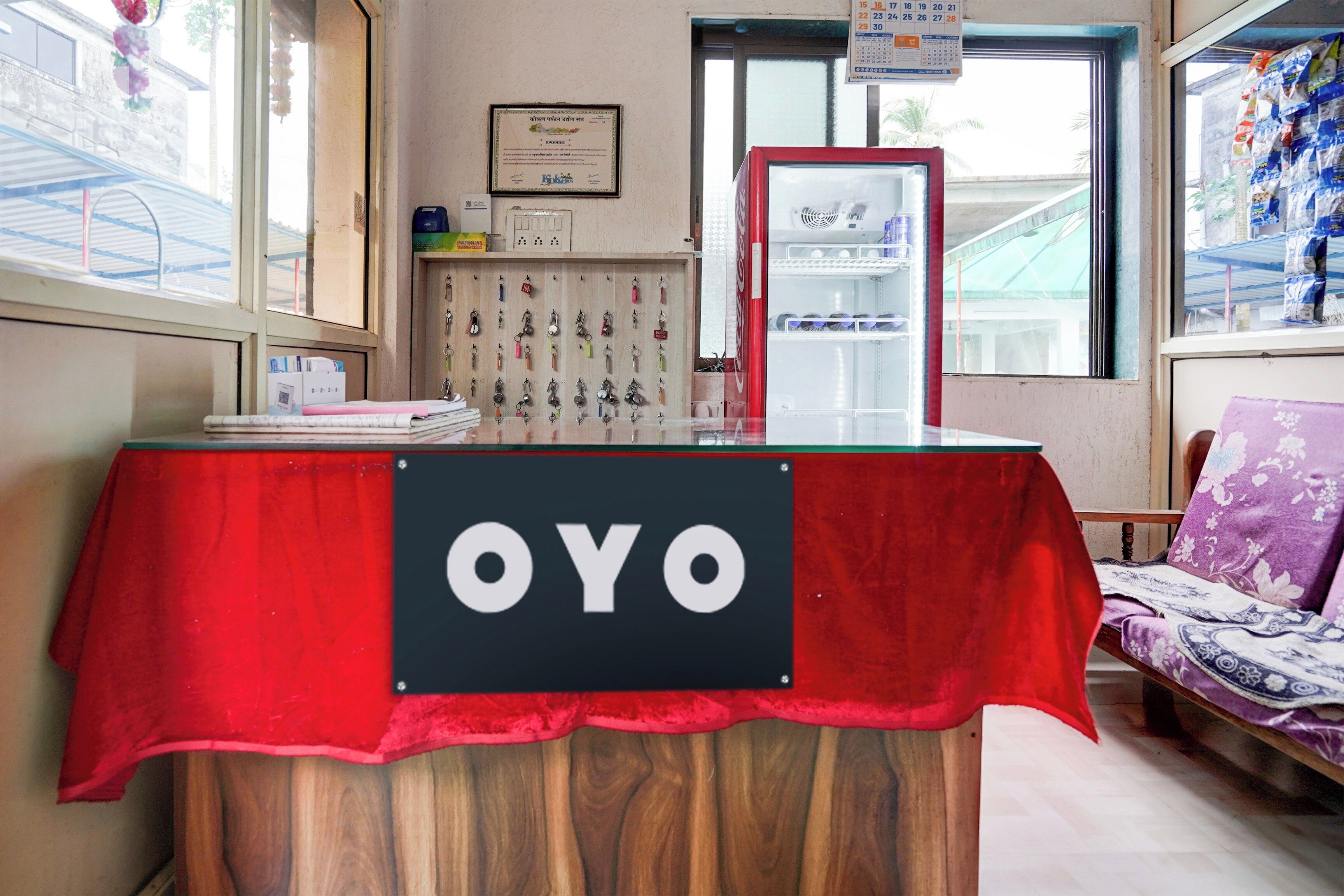 A reception desk with a red tablecloth, a sign reading 'OYO', and a calendar on the wall.