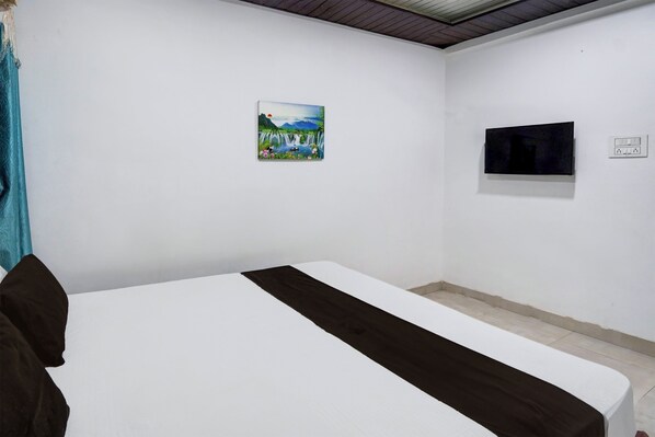 A room with a bed, a painting on the wall, a television, and a power outlet.
