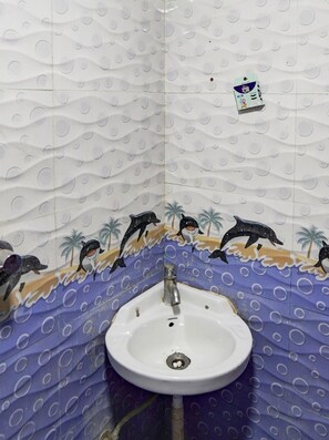 A bathroom with a white sink, decorative tiles featuring dolphins and palm trees, and a small soap dispenser on the wall.