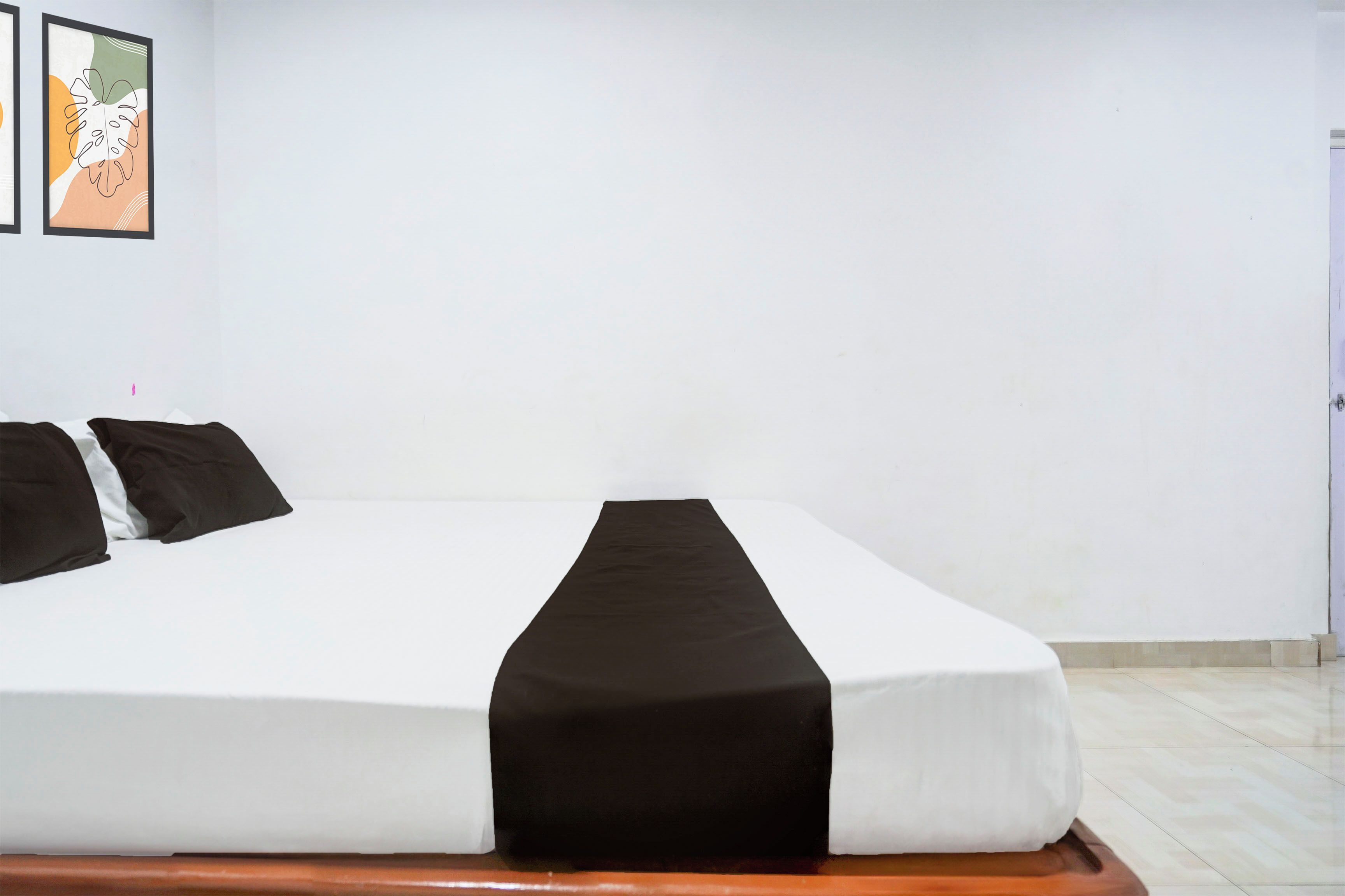 Un lit avec un matelas blanc et une couvre-lit noire, deux oreillers noirs et une tête de lit en bois.