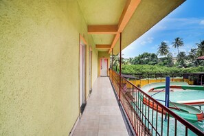 A corridor leading to a pool area with a view of palm trees and a clear sky. - Hotel O Raj Resort (Vasai)