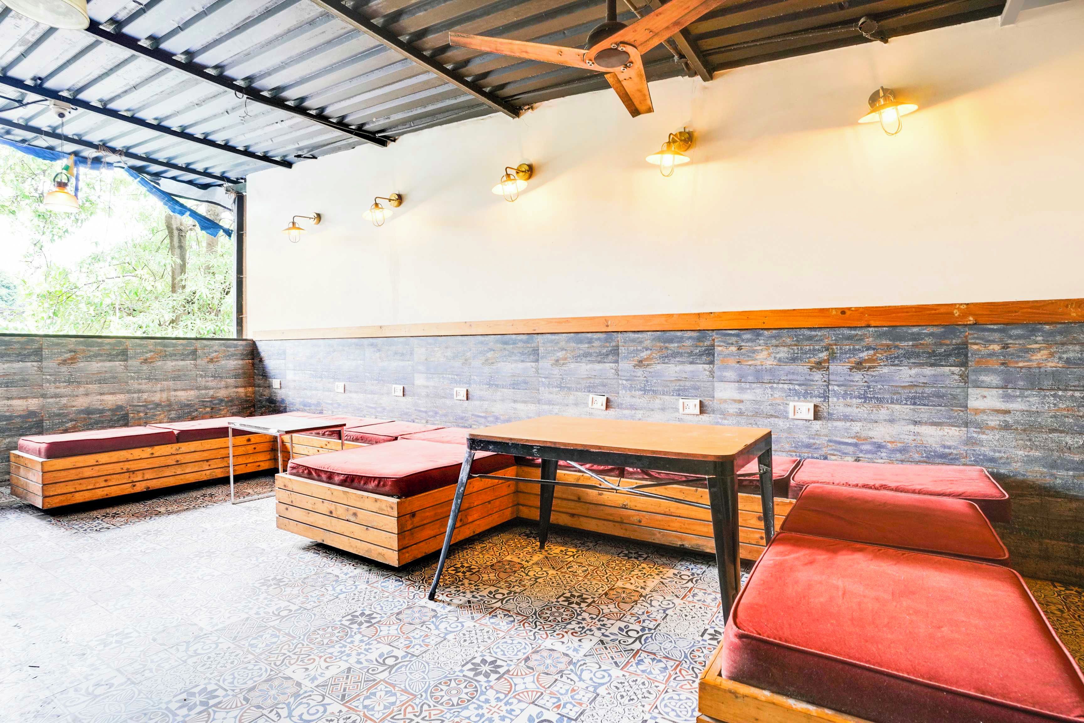 Interior de restaurante con techo alto, vigas a la vista y una variedad de opciones de asientos, incluyendo bancos y una mesa.
