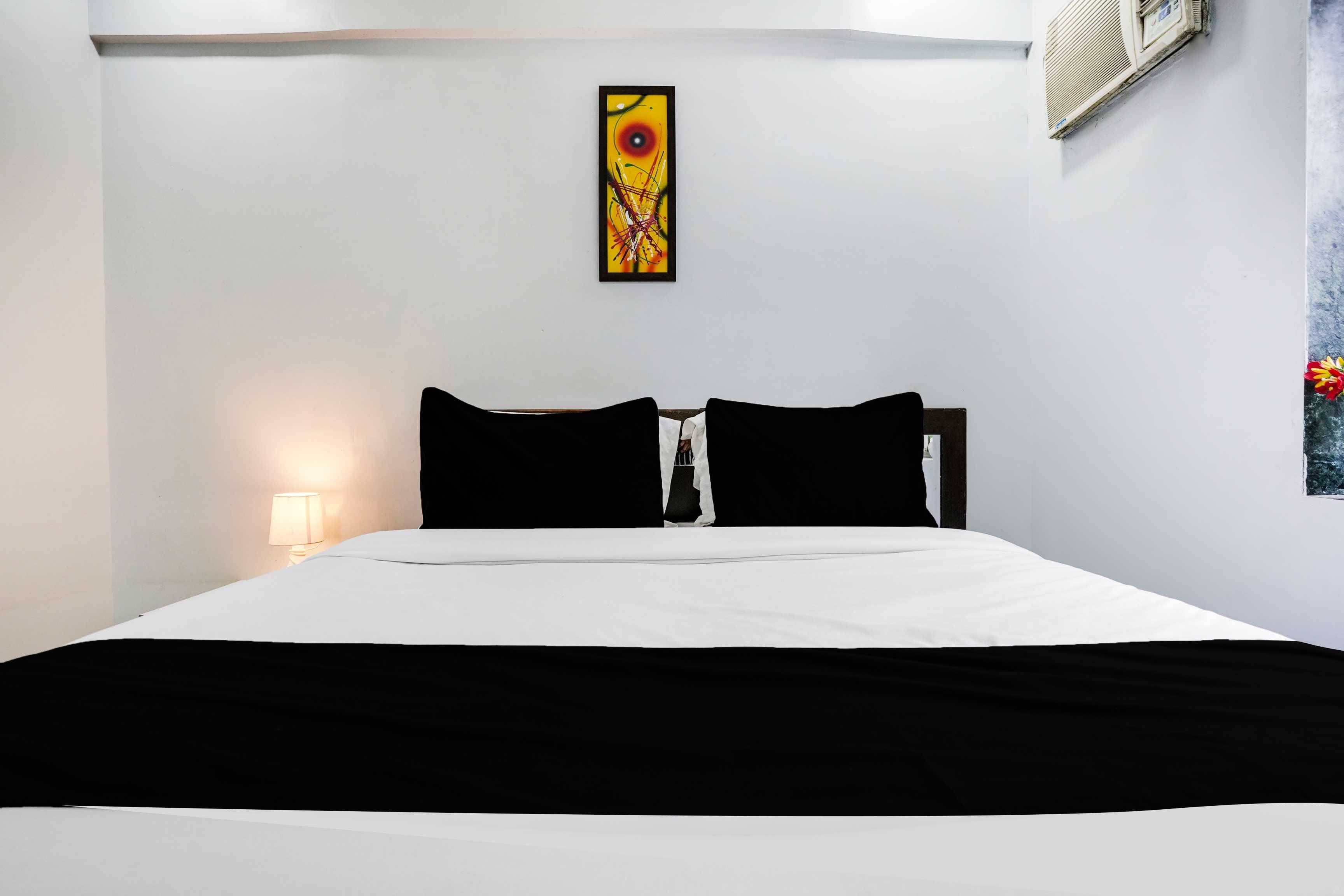A hotel room with a bed, a nightstand, a lamp, and a painting on the wall.