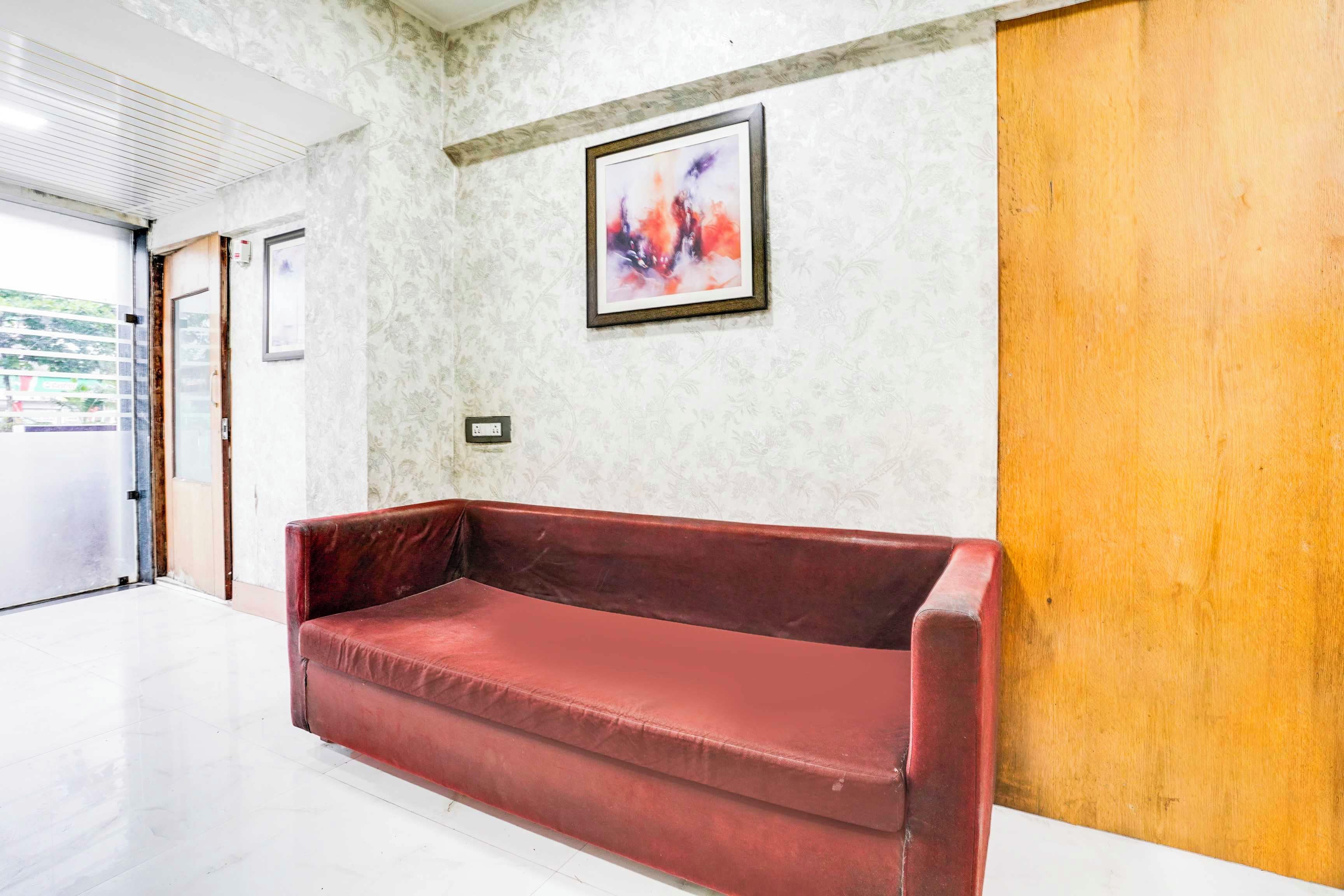 A red sofa in a hallway with patterned wallpaper, a framed abstract painting, and a wooden door.