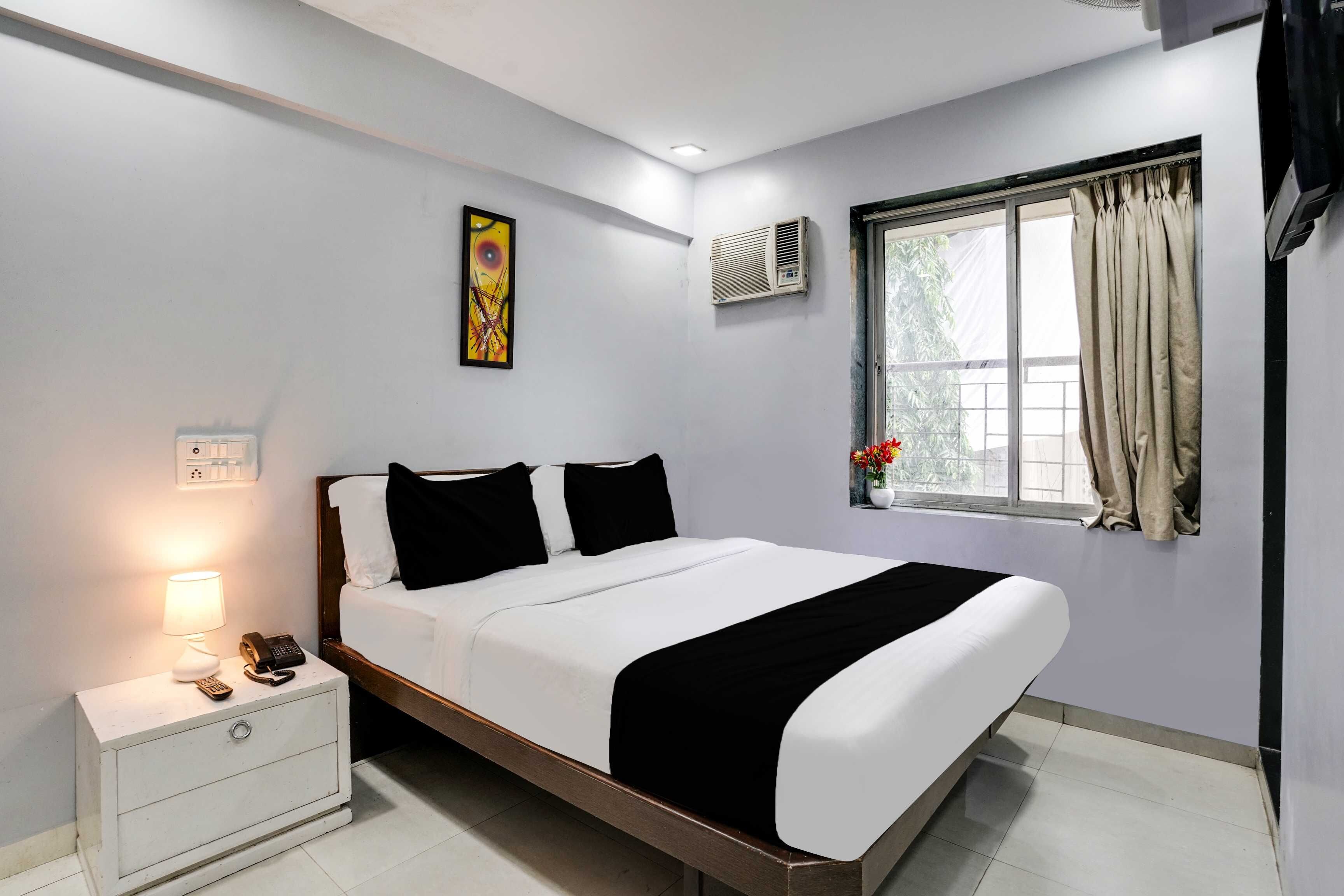 Una habitación de hotel moderna con cama, mesita de noche, lámpara, equipo de aire acondicionado y ventana con cortinas.