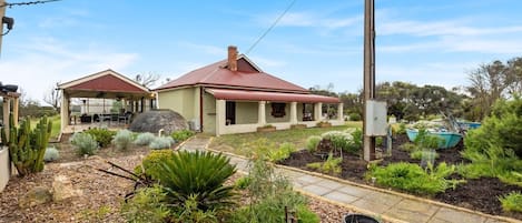 A house with a red roof, a covered patio, and a garden with various plants and a cactus.