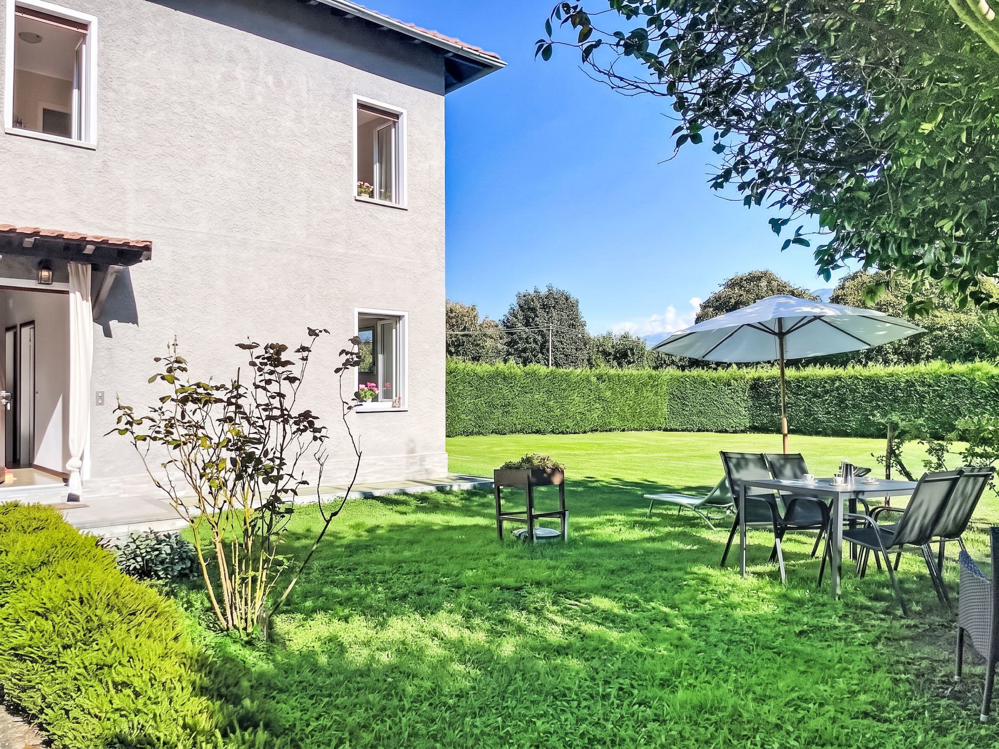 A house with a patio area, a table with chairs, and a large umbrella.