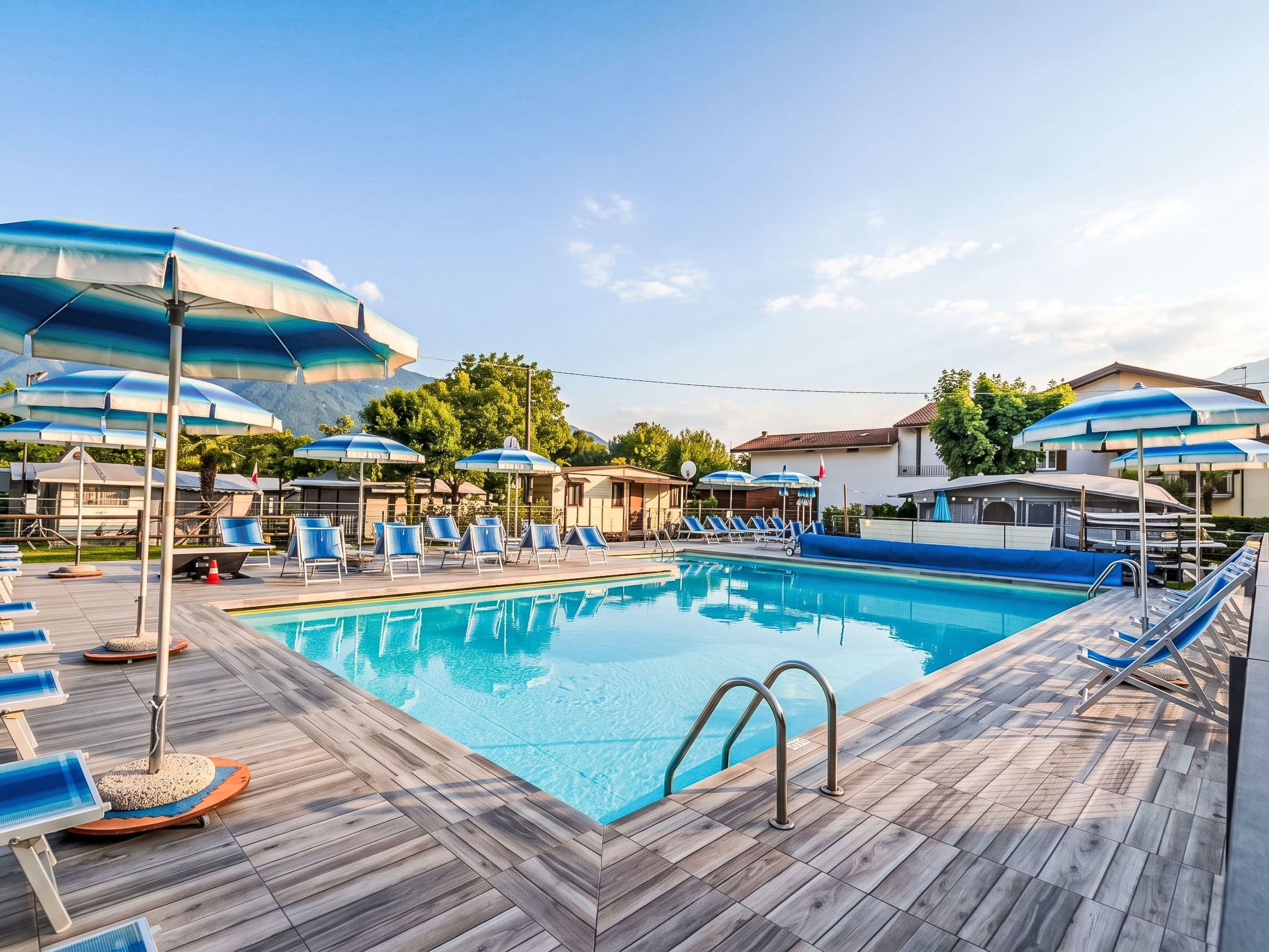 A swimming pool with lounge chairs and umbrellas, surrounded by buildings and trees.