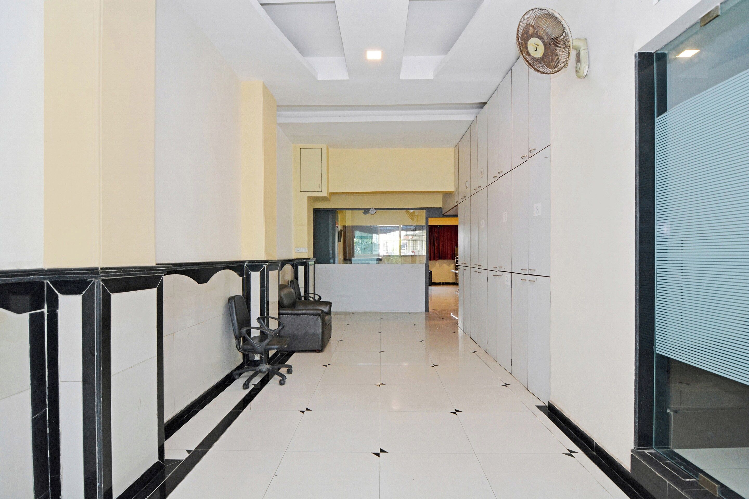 A hallway with a tiled floor, a black and white railing, and a row of cabinets on one side.