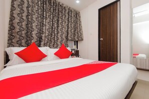 A hotel room with a bed, two red pillows, a red throw, a wooden wardrobe, and a patterned curtain. - Hotel O Gems (Mumbai)