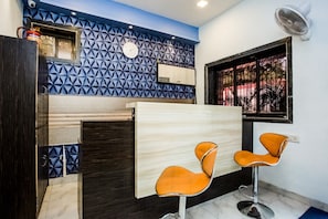 Un interior moderno con una pared de estampado geométrico, un reloj, una ventana con vistas y dos sillas color naranja.