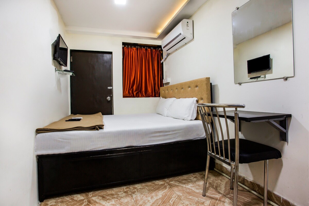 Habitación de hotel compacta con cama, escritorio, silla, aire acondicionado, televisor y puerta.