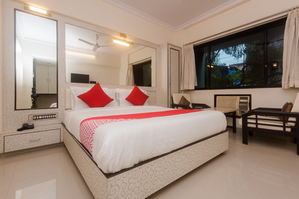 A hotel room with a large bed, two bedside tables, a desk, a chair, and a window with curtains.
