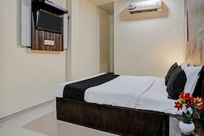 Quarto de hotel com cama, televisão fixada na parede, aparelho de ar condicionado e planta em vaso.