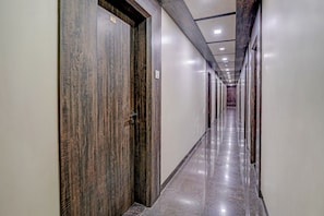 Um corredor comprido e estreito com portas de madeira e chão de mármore brilhante.