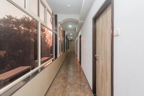 Un pasillo con suelo de baldosas, puertas de madera y ventanas que reflejan árboles.