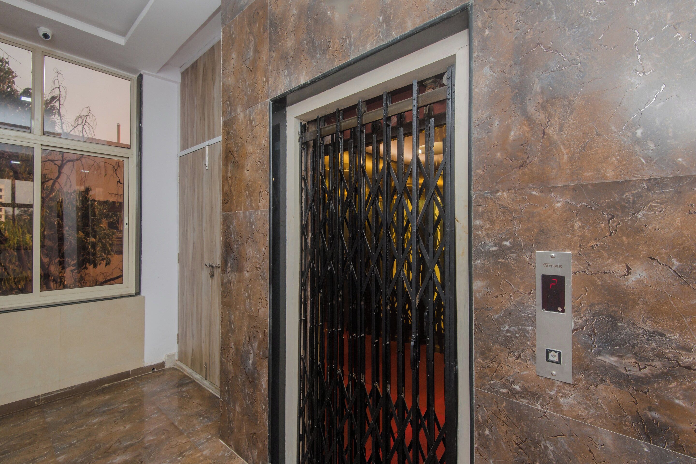 Un ascensor con pantalla digital, una puerta metálica y una pared de mármol.