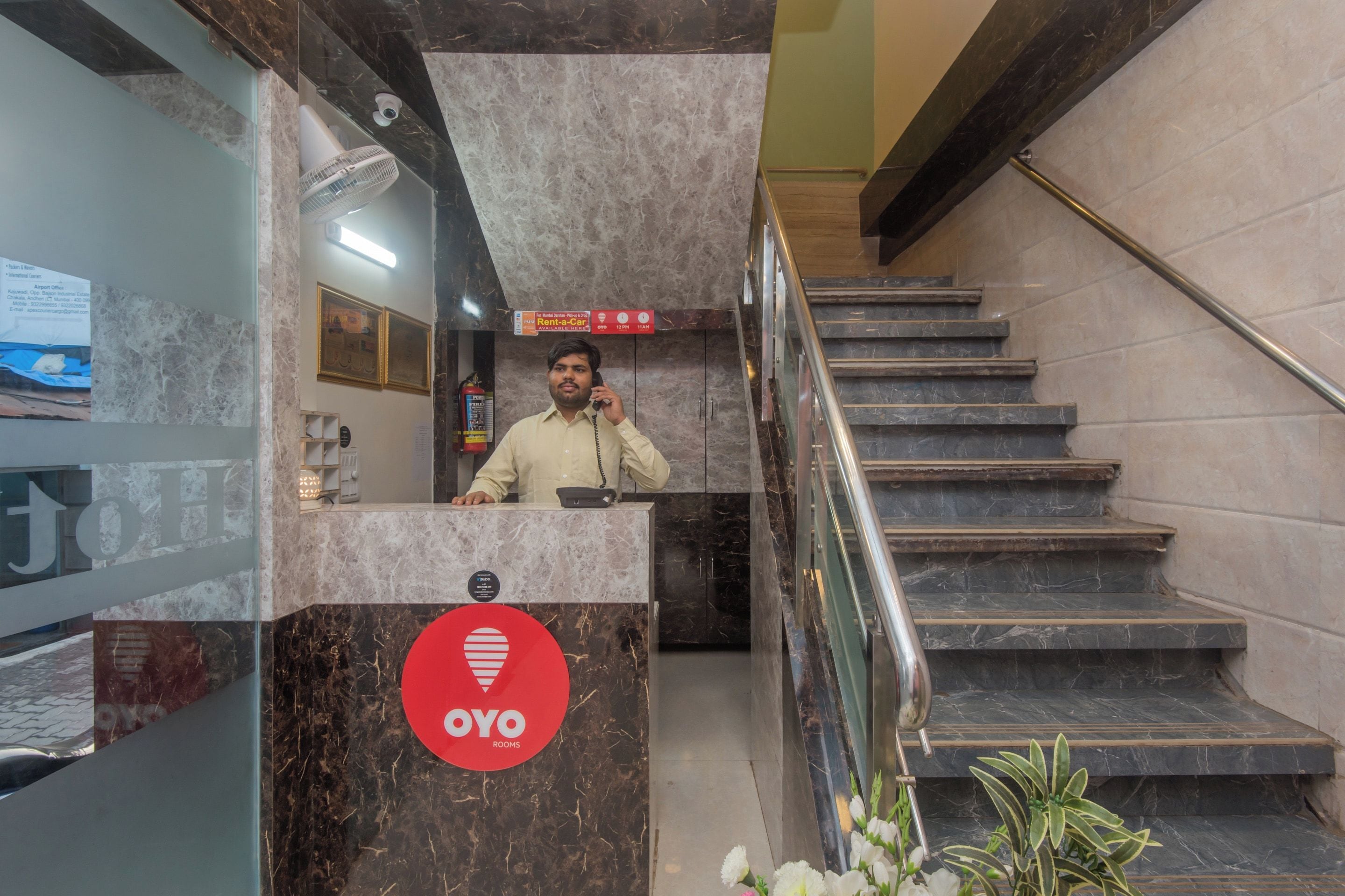 A hotel reception area with a marble counter, a staircase, and a sign indicating 'OYO ROOMS'.