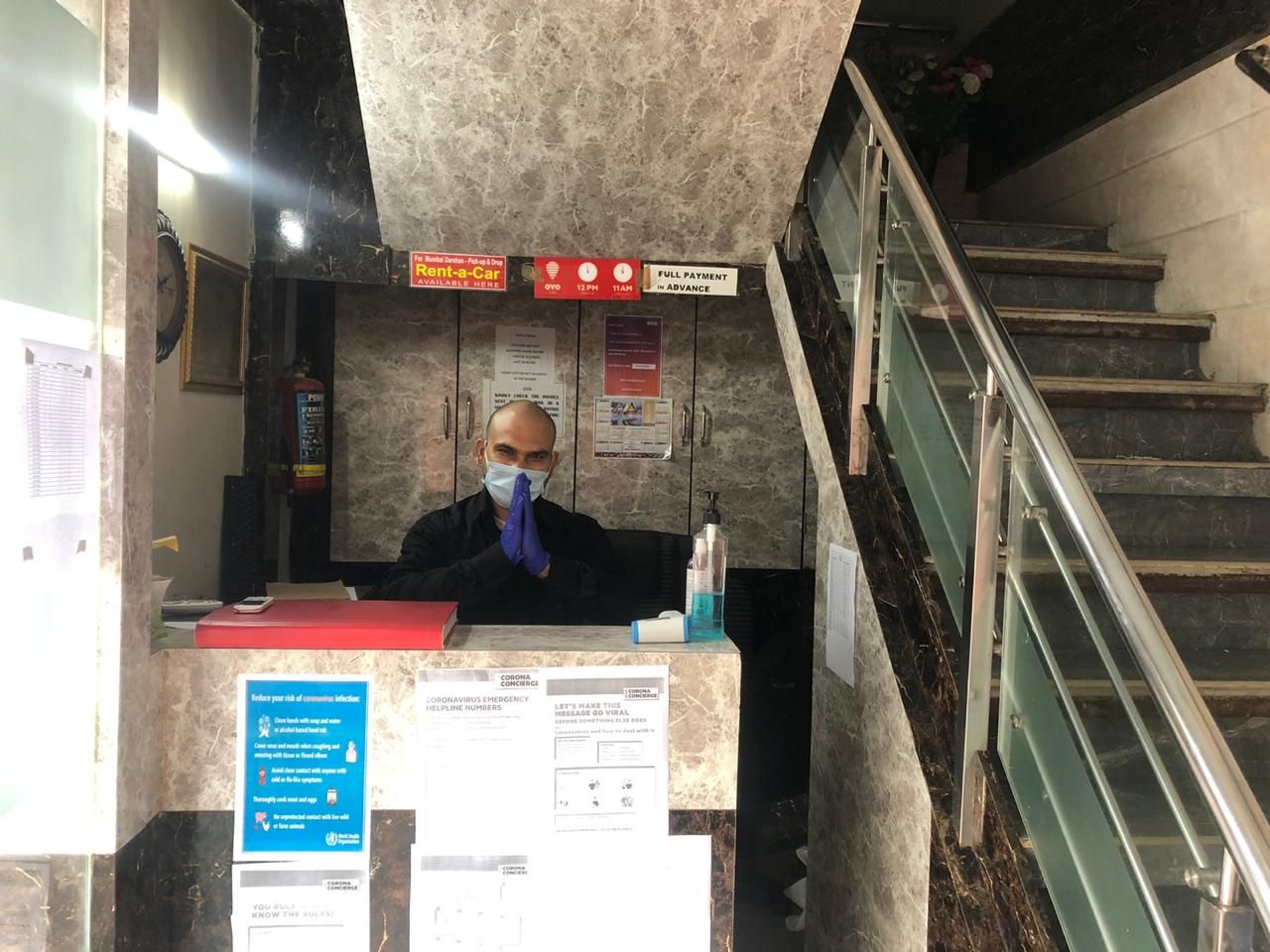 A reception desk with a person behind it, a sign for a Rent-a-Car service, and emergency contact numbers.