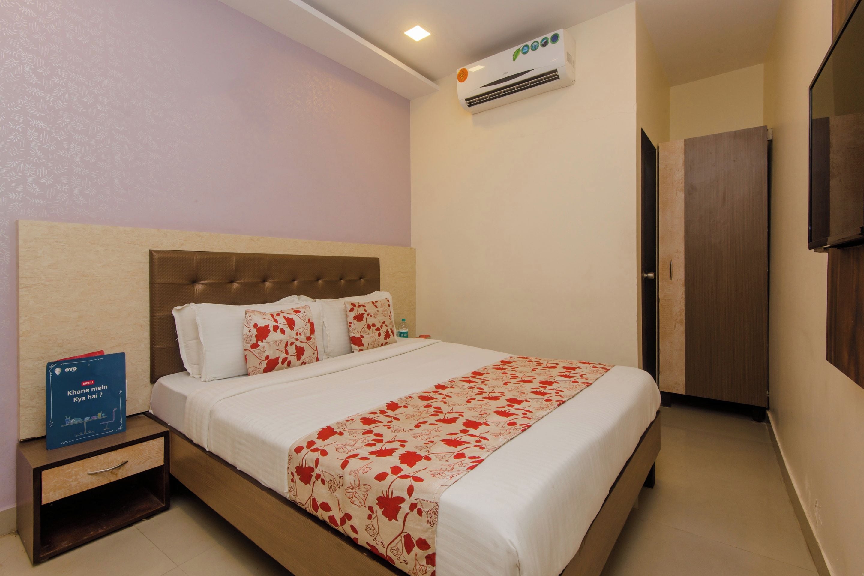 Habitación de hotel con una cama, una mesita de noche, aire acondicionado en la pared y una puerta.