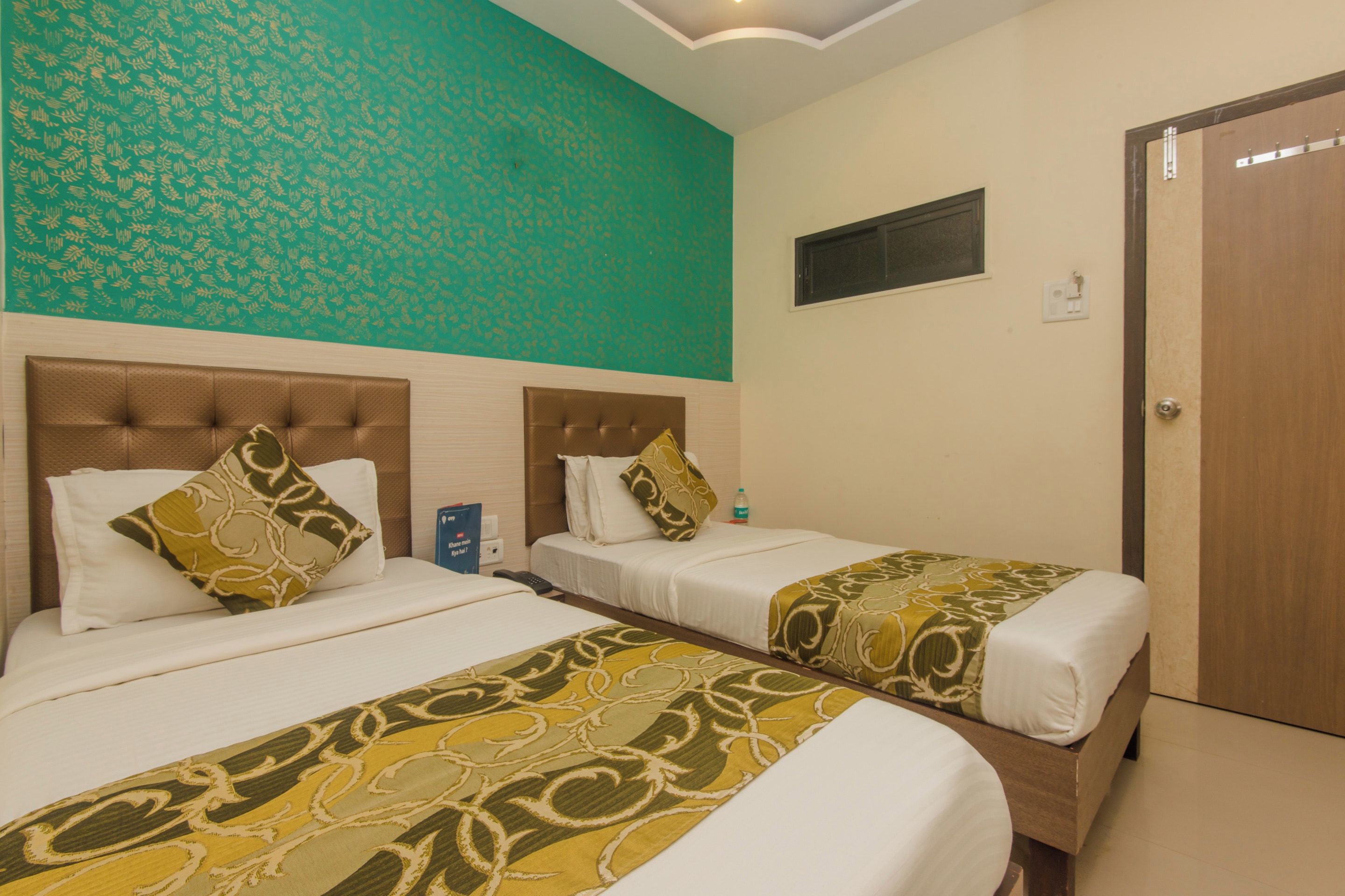 Una habitación de hotel con dos camas, una pared color esmeralda con estampado y una puerta de madera.