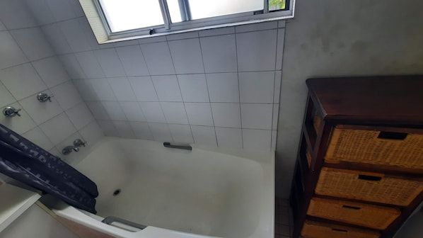 Casa de banho com banheira, janela e paredes revestidas a azulejos.