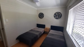 Quarto pequeno e compacto com duas camas de solteiro, um ventilador de teto e dois objetos decorativos presos à parede.