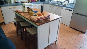 Een keuken met een centraal kookeiland, stoelen, een fornuis en verschillende etenswaren.