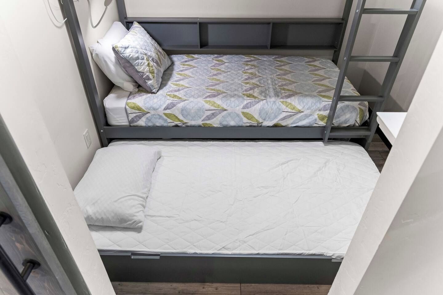 A bunk bed with a patterned bedspread and pillows, a lower bunk with a plain mattress, and a ladder attached to the side.