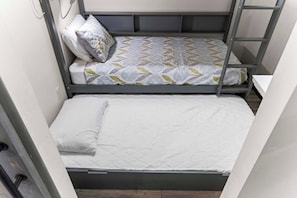 Ein Etagenbett mit einem gemusterten Bettbezug und Kissen, die untere Etage mit einer schlichten Matratze, und eine an der Seite befestigte Leiter.