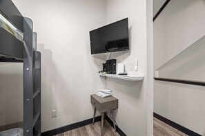 Ein kleines Zimmer mit einem Etagenbett, einem an der Wand befestigten Fernseher, einem Tisch mit Handtuch und einem Regal mit elektronischen Geräten.