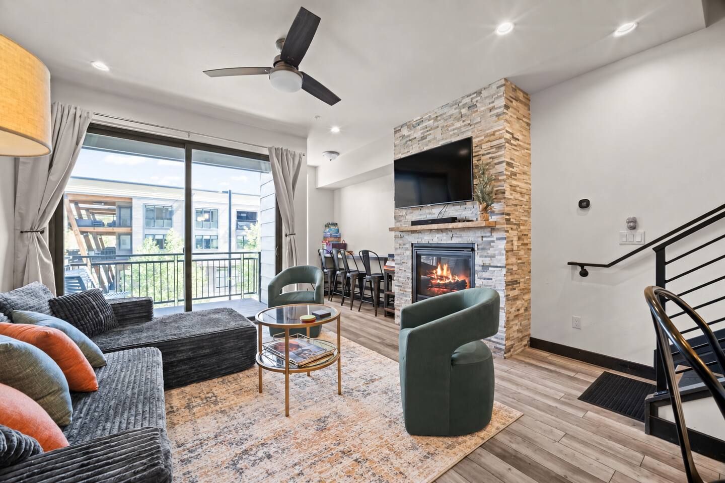 A modern living room with a fireplace, a ceiling fan, and a view of the outside.