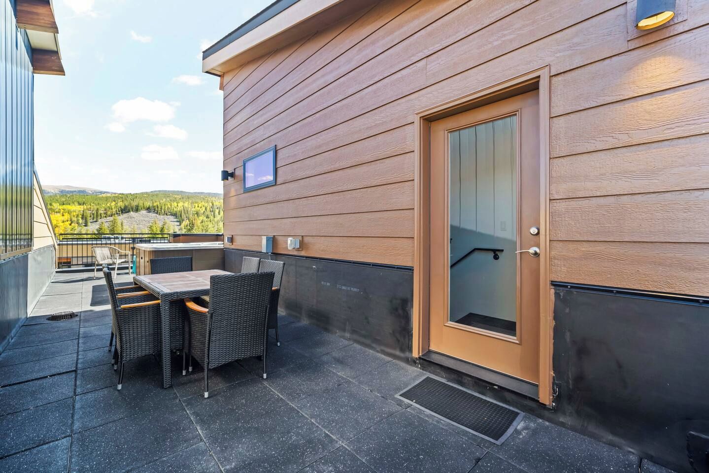 Un bâtiment moderne avec une façade en bois, une porte dotée d’un panneau de verre et un patio aménagé avec du mobilier d’extérieur.