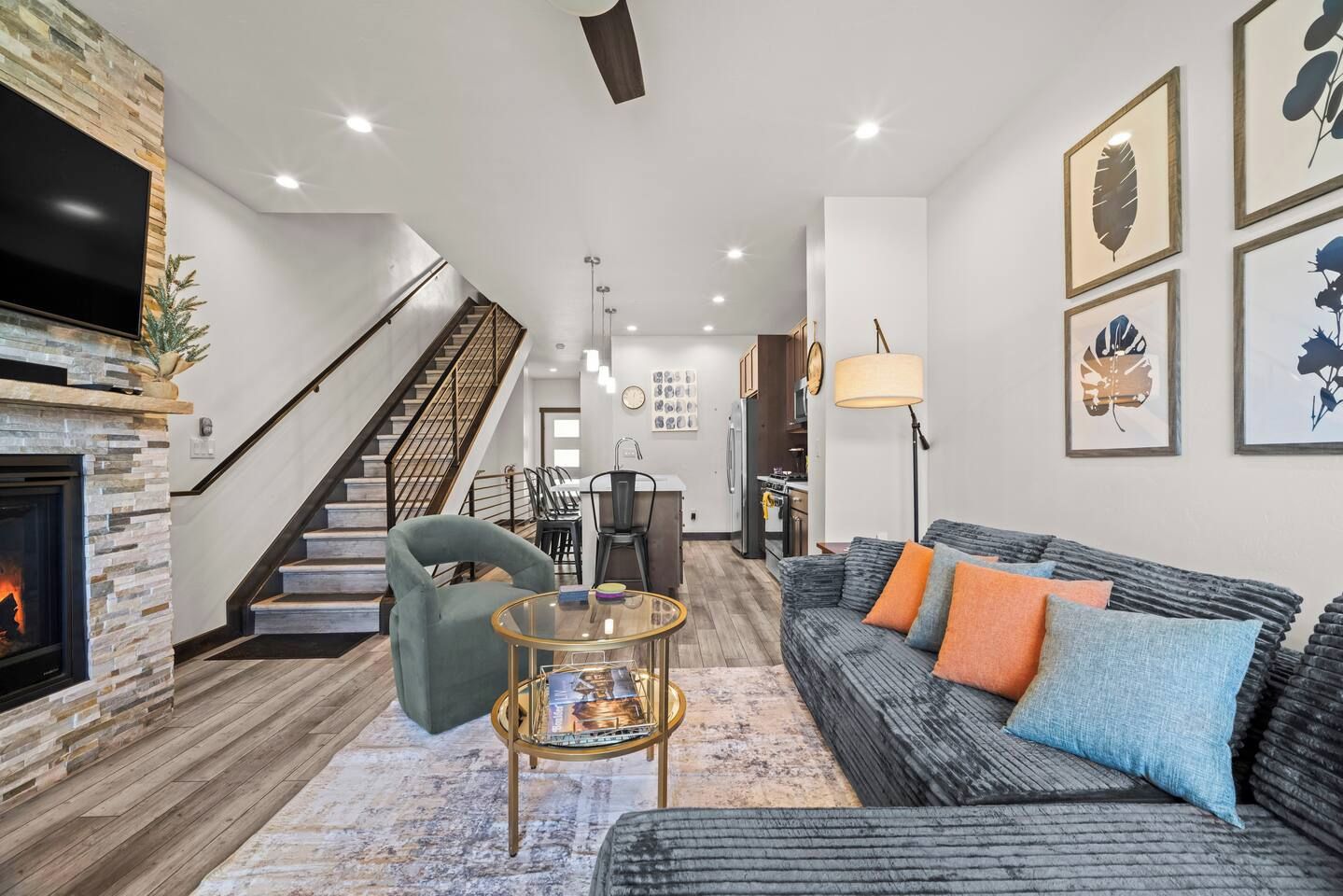A modern living room with a fireplace, a staircase, a dining area, and a kitchen.
