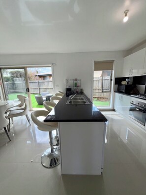 A modern kitchen with a central island, white cabinetry, and a dining area with white chairs.