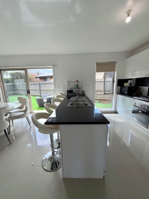 A modern kitchen with a central island, white cabinetry, and a dining area with white chairs.
