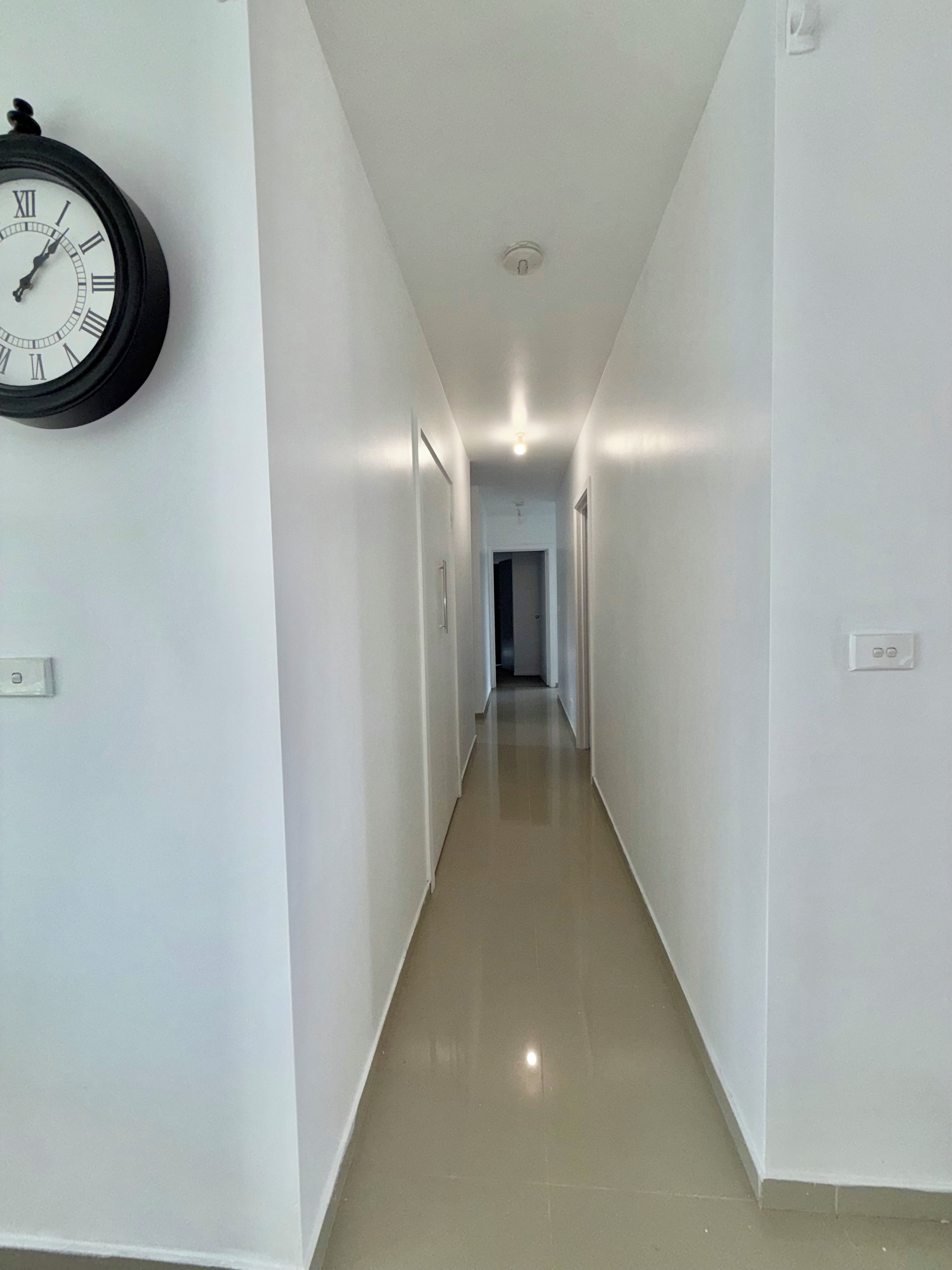 A corridor with a clock on the wall, leading to a door at the end.