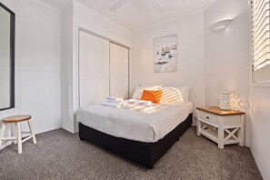 Une chambre à coucher avec un lit, une table de chevet, un tabouret et un tableau accroché au mur.