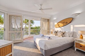 Un dormitorio con cama, ventilador de techo, una tabla de surf en la pared y un balcón con puertas correderas.