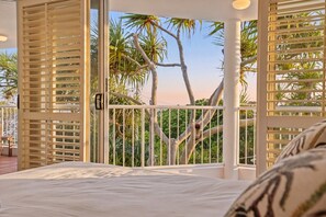 Une chambre avec un grand lit, une vue sur des palmiers et un balcon doté d’une balustrade.