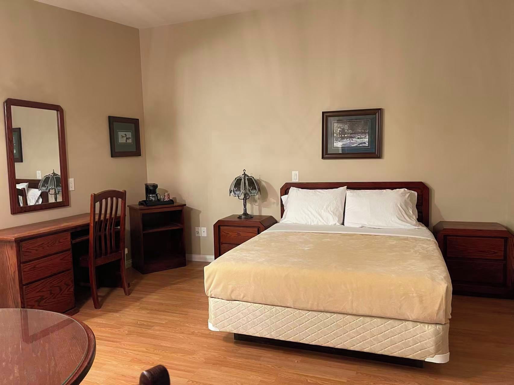 A hotel room with a bed, a desk, a chair, a lamp, and a mirror.