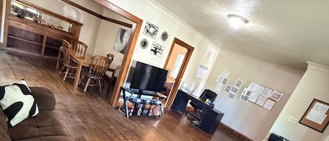 Un salon avec un grand canapé marron, un coin repas avec des chaises en bois et une cuisine équipée d’un réfrigérateur et d’un four à micro-ondes.