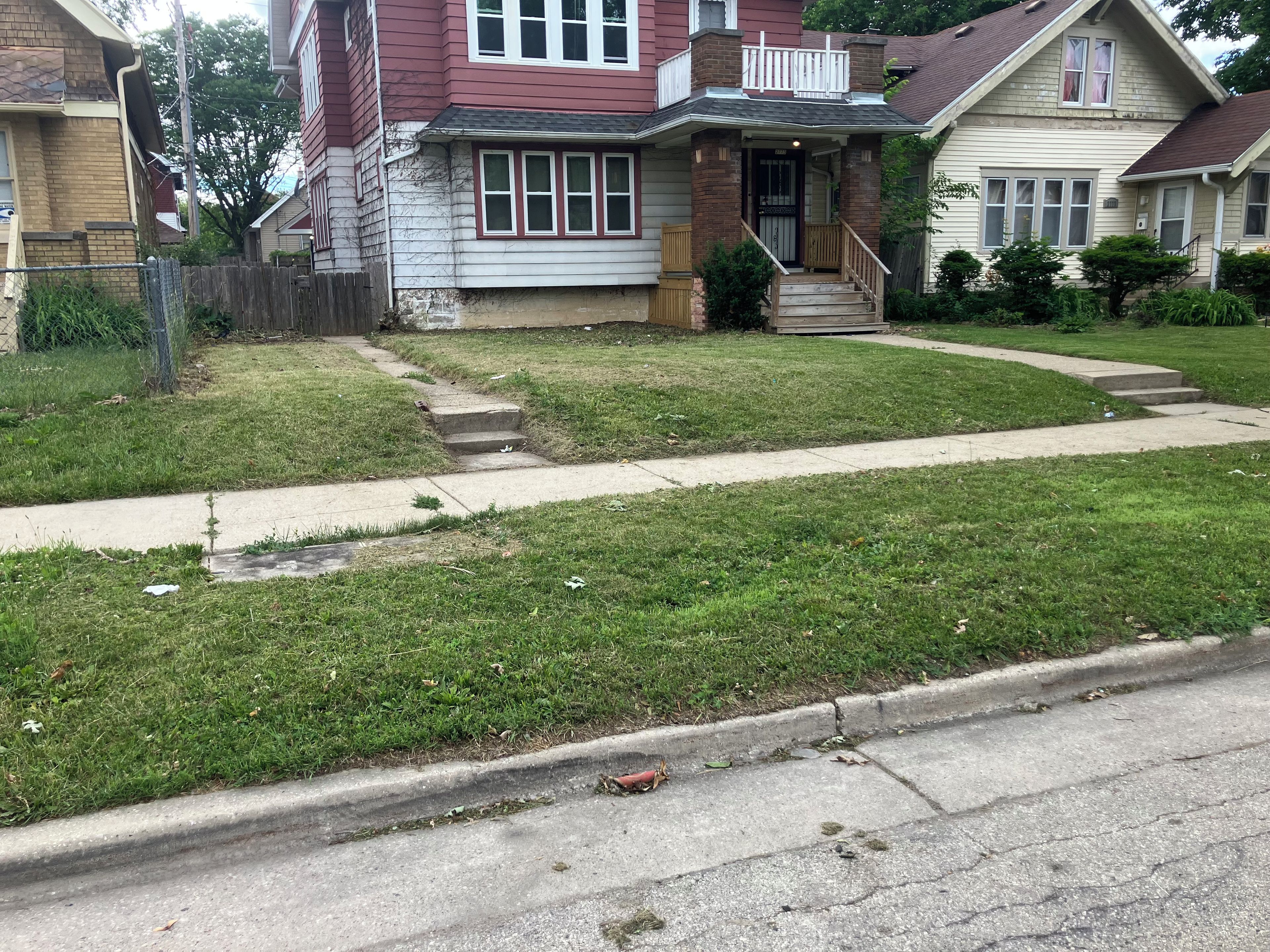 Une rue résidentielle bordée de maisons, avec un trottoir et une zone herbeuse.