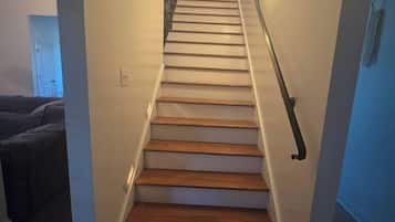 Un escalier avec des marches en bois et une rampe, menant à un palier où se trouve un luminaire.