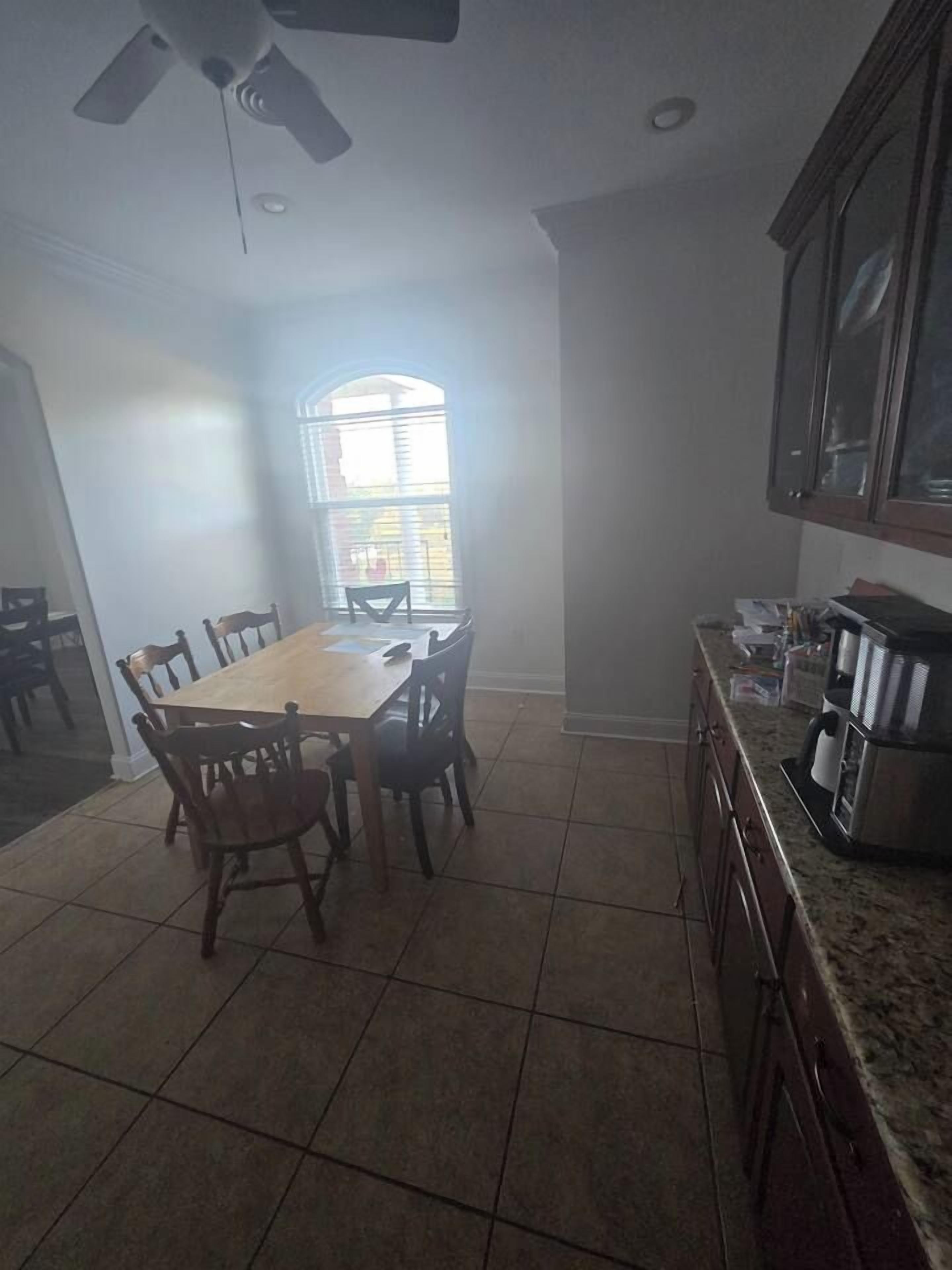 Un comedor con mesa y sillas de madera, ventilador de techo y zona de cocina con armarios y electrodomésticos.