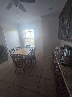 A dining area with a wooden table and chairs, a ceiling fan, and a kitchen area with cabinets and appliances.