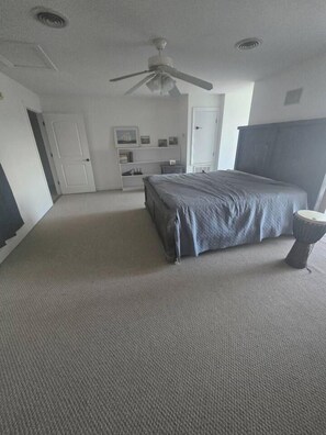 A bedroom with a bed, a ceiling fan, a door, and a small table.